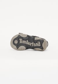 Μαύρη σόλα υποδημάτων Timberland με υφή, κατασκευασμένη από ελαστικό υλικό, και με έντονο σχέδιο. Διαθέτει διακριτικά γκρίζα στοιχεία και το χαρακτηριστικό λογότυπο "Timberland".