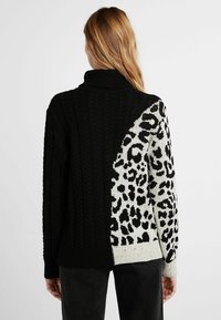 Chandail noir en tricot avec un col haut, présentant un motif de câble texturé d'un côté et un imprimé léopard de l'autre.
