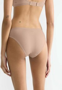 Beige, nahtlose Unterwäsche mit glatter Textur, mittelhohem Schnitt und elastischem Bund. Mit Markenlogo auf der Rückseite.