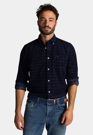 Navyblauw geruit overhemd van katoen met een button-down kraag, voorzien van een borstzak en opgerolde mouwen, gedragen met blauwe spijkerbroek.