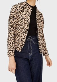 Giacca in stampa leopardata beige, caratterizzata da un colletto rotondo, maniche lunghe e un design corto. Abbinata a jeans blu a vita alta.