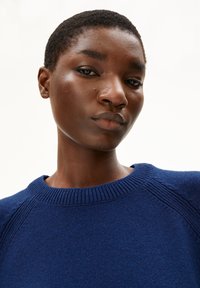 Navy knit sweater with a ribbed crew neckline and raglan sleeves. Features a textured pattern and is made from a thick, soft fabric.