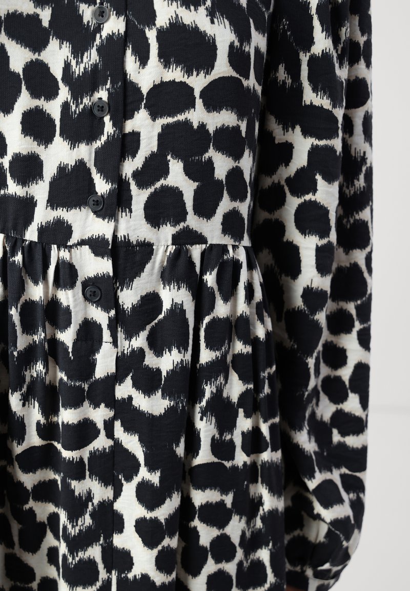 Schwarzes und weißes Leopardenmuster-Kleid mit durchgeknöpften Vorderteil, plissiertem Rock, langen Ärmeln und strukturiertem Stoff.