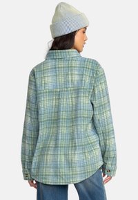 Grønternet flannel skjorte med en afslappet pasform, der har store ternede mønstre, en krave og knapmanchetter. Båret med en stribet hue.