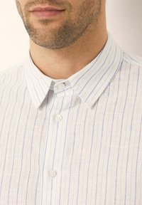 Bílá lněná košile s světle modrými vertikálními pruhy, s límečkem na knoflíky a dvěma předními knoflíky, s texturovaným povrchem.