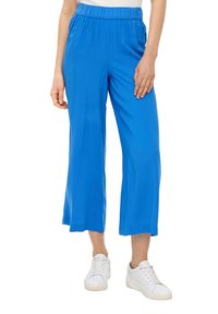 Blauwe, wijde broek van lichtgewicht stof met een elastische tailleband, gecombineerd met witte sneakers.