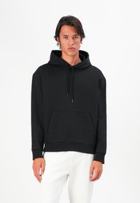 Svart hettegenser med kænguru-lomme, laget av mykt stoff. Har justerbare snorer og ribbede mansjetter for en tettsittende look.