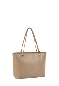 Beżowa torba typu tote z ekoskóry z dwoma uchwytami, srebrnymi metalowymi elementami i okrągłym, ozdobionym ćwiekami logo na przodzie. Gładka faktura i wyraźnie zarysowany kształt.