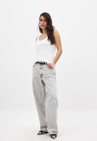 Witte geribbelde tanktop gecombineerd met losse lichtgrijze jeans. Accessoires omvatten een zwarte riem en witte armbanden. Schoeisel heeft zwart-witte strepen.