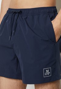 Costumi da bagno blu navy con vita elastica, chiusura con cordino, due tasche laterali e una patch con logo bianco sulla parte bassa della gamba sinistra.