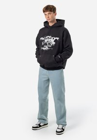 Schwarzer Hoodie mit weißem Grafikdruck, lässige Passform und Kängurutasche. Hellblaue gerade Jeans und Schwarz-Weiß-Sneaker.