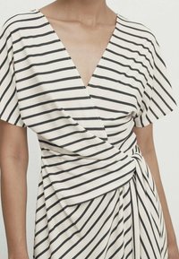 Randig omslagsklänning med djup V-ringning, korta ärmar, tillverkad av lättviktsmaterial. Har horisontella ränder i marinblått på en krämfärgad bakgrund.