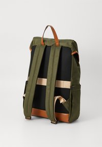 Sac à dos vert olive avec des accents en cuir brun, des bretelles réglables, un dos en tissu noir texturé et des poches latérales pour un rangement supplémentaire.
