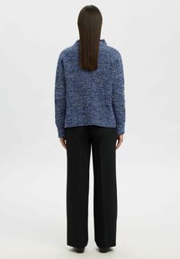 Maglione blu texturizzato con colletto, abbinato a pantaloni neri a gamba larga. Il maglione ha una vestibilità ampia e un motivo di lavorazione ben visibile.