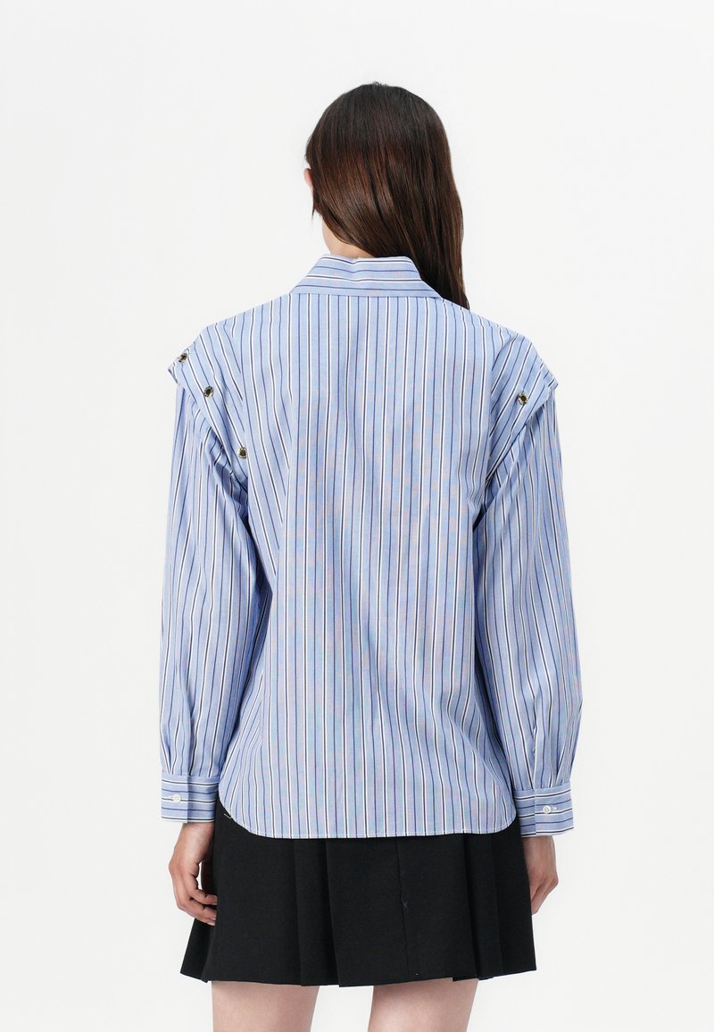 Gestreept blouse in lichtblauw en wit met opgeblazen mouwen; heeft schouderknopen en een afgeronde zoom; gecombineerd met een korte zwarte rok.