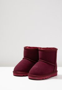 Botas de tobillo de ante burdeos con un suave forro de felpa, que cuentan con una puntera redondeada y suela de goma texturizada con un borde serrado.