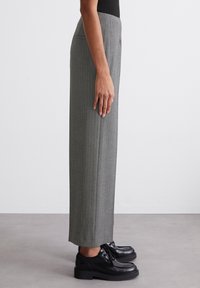 Graue gestreifte Hose mit hoher Taille, taillierter Passform und weitem Bein, kombiniert mit schwarzen Leder-Schnürschuhen. Glatte Textur.