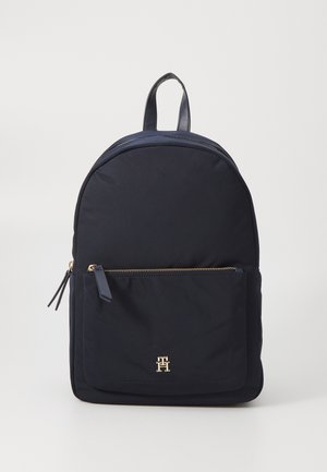 Mochila de nailon azul marino con forma redondeada, que presenta un bolsillo frontal con cremallera dorada y herrajes en contraste dorado. Incluye una asa de transporte en la parte superior.