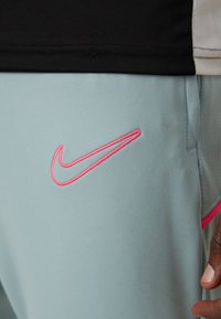 Lysblå sportshorts med et pink Nike-logo, lavet af tekstureret stof med et mesh-panel og flad sort talje.