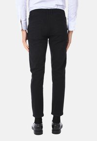 Pantaloni neri slim-fit con una finitura di tessuto liscia. Dotati di tasche posteriori e di una vita con passanti per la cintura. Abbinati a scarpe nere.