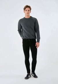 Sudadera gris de manga larga, jeans negros ajustados y zapatillas negras. El conjunto presenta un diseño sencillo y una textura suave.