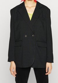 Černý kostkovaný oversized blazer s modrými pruhy, dvojřadové knoflíky, zářezovými klopami a dvěma předními kapsami. Hladká textura.