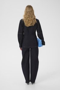 Tumša džinsa jaka ar pielāgotu piegriezumu, redzamas šuvju detaļas un pogātas aproces, kombinēta ar platām tumša džinsa biksēm un gaiši zilu rokassomiņu.