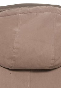 Tejido de chaqueta rosa claro con una textura suave, que cuenta con una capucha parcialmente visible y un meticuloso acabado en las costuras.