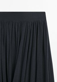 Black pleated skirt with wide elastic waistband, showing gathered fabric texture and vertical folds.