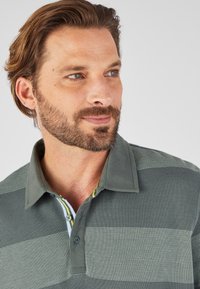 Groen gestreepte polo met een gestructureerde stof, knoopsluiting en een kleurrijke kraag met gele en blauwe accenten.