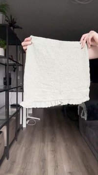 Šviesiai žalia tekstūruota medžiaga su raukšlėta apatine dalimi laikoma aukštai. Medžiaga turi subtilų raštą ir minkštą, suglebusį išvaizdą.