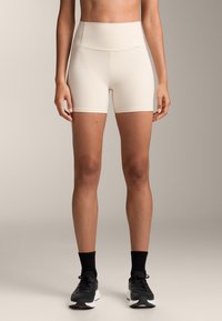 Béžové šortky s vysokým pásom, hladkou textúrou, priliehavým strihom a čistými líniami, skombinované s čiernymi športovými topánkami a ponožkami s výškou do členkov.