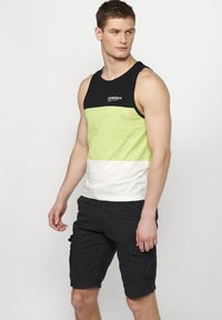 Žalias, juodas ir baltas dryžuotas rankovių neturintis marškinėlis, pagamintas iš minkštos medžiagos, derinamas su juodais cargo šortais, turinčiais šonines kišenes ir laisvą siluetą.