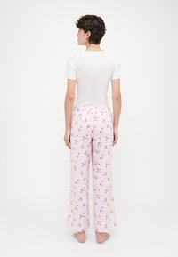 Top bianco a maniche corte abbinato a pantaloni a quadri rosa chiaro con stampa floreale in accenti rossi e verdi. Vestibilità ampia e vita elastica.