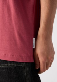 Tricou din bumbac de culoare burgundă, cu mâneci scurte, etichetă laterală și o textură netedă, asortat cu blugi din denim închisi la culoare, cu cusături contrastante.