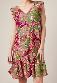 Vestido con estampado floral que presenta un escote en V, mangas con volantes y un dobladillo acampanado. Los colores dominantes son rosa, verde y púrpura, y está hecho de una tela ligera.