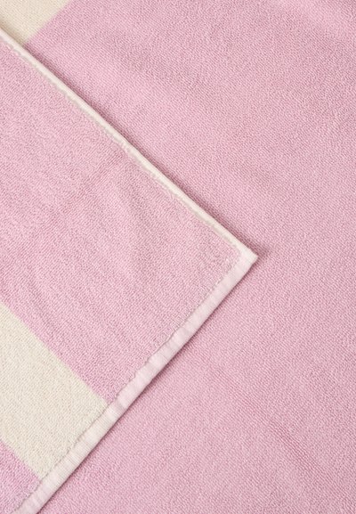 Serviette rose douce avec un coin replié montrant une bande crème le long du bord sur un fond en tissu rose assorti.