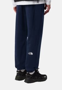 Pantalones de chándal azul marino con puños elásticos, fabricados en material suave. Presentan el logo blanco de "The North Face" en el muslo izquierdo.