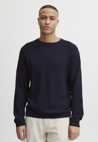 Pulover tricotat bleu marin, cu manșoni lungi, decolteu rotund și tivuri cu nervuri. Textură netedă, cu un design ajustat și mâneci raglan.
