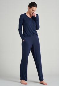 La camiseta de manga larga en navy presenta un escote estilo henley con tres botones. Se combina con pantalones holgados a juego, ambos de una suave y texturada tela.