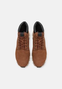 Calzado de cuero marrón con forro interior negro, puntera redonda y suelas gruesas blancas. Presenta cordones marrones y un logotipo en la lengüeta.