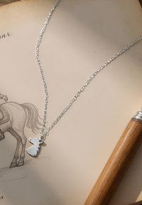 Sølv kædedyne med en hestehoved vedhæng. Kæden har et struktureret leddesign. Sat mod en lys papirbaggrund med en skitse.