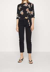 Blusa nera a fiori con maniche a tre quarti, dotata di un fiocco laterale. Abbinata a pantaloni neri a sigaretta e sandali neri con cinturini.