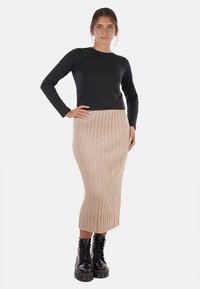 Maglietta nera a maniche lunghe abbinata a una gonna midi beige a coste, indossata con stivali neri con lacci e zeppa. Elementi di design semplici e pieni di texture.