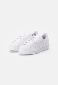 White sneakers with a textured leather upper, rubber shell toe, and three stripe design. Lace-up closure and padded collar for comfort.