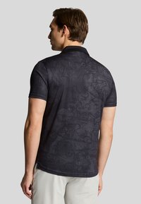 Korte ærmer polo shirt i sort med et struktureret paisley mønster og krave. Materialet har en glat finish og er forsynet med sideslidser i kanten.