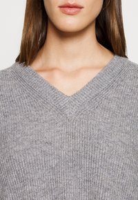 Maglione grigio a V con texture a coste, caratterizzato da un fit rilassato e design senza cuciture. Il materiale appare morbido e leggermente elasticizzato.