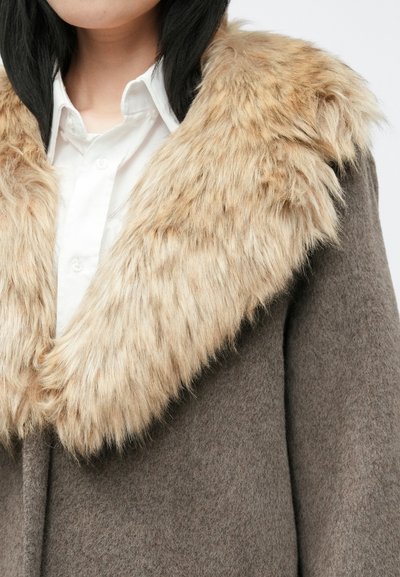 Καφέ μάλλινο παλτό με μεγάλο κολάρο από τεχνητό γούνινο υλικό σε ανοιχτό καφέ χρώμα. Το ύφασμα είναι μαλακό με απαλό άγγιγμα, σε αντίθεση με το φουντωτό κολάρο.