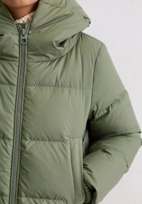 Kurtka puchowa w kolorze oliwkowej zieleni z kapturem, posiadająca przedni zamek błyskawiczny i pikowany wzór przeszyć. Miękki materiał, teksturowana tkanina oraz wyraźny kołnierz.