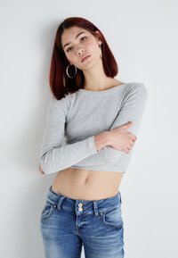 Svijetlosivi dugi rukav krojeni top s okruglim izrezom i rebrastom teksturom, u kombinaciji s plavim trapericama visokog struka s detaljima gumba.